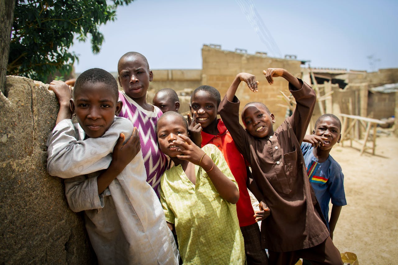 A group of children expressing joy outdoors in Kano, Nigeria, against a rustic backdrop.